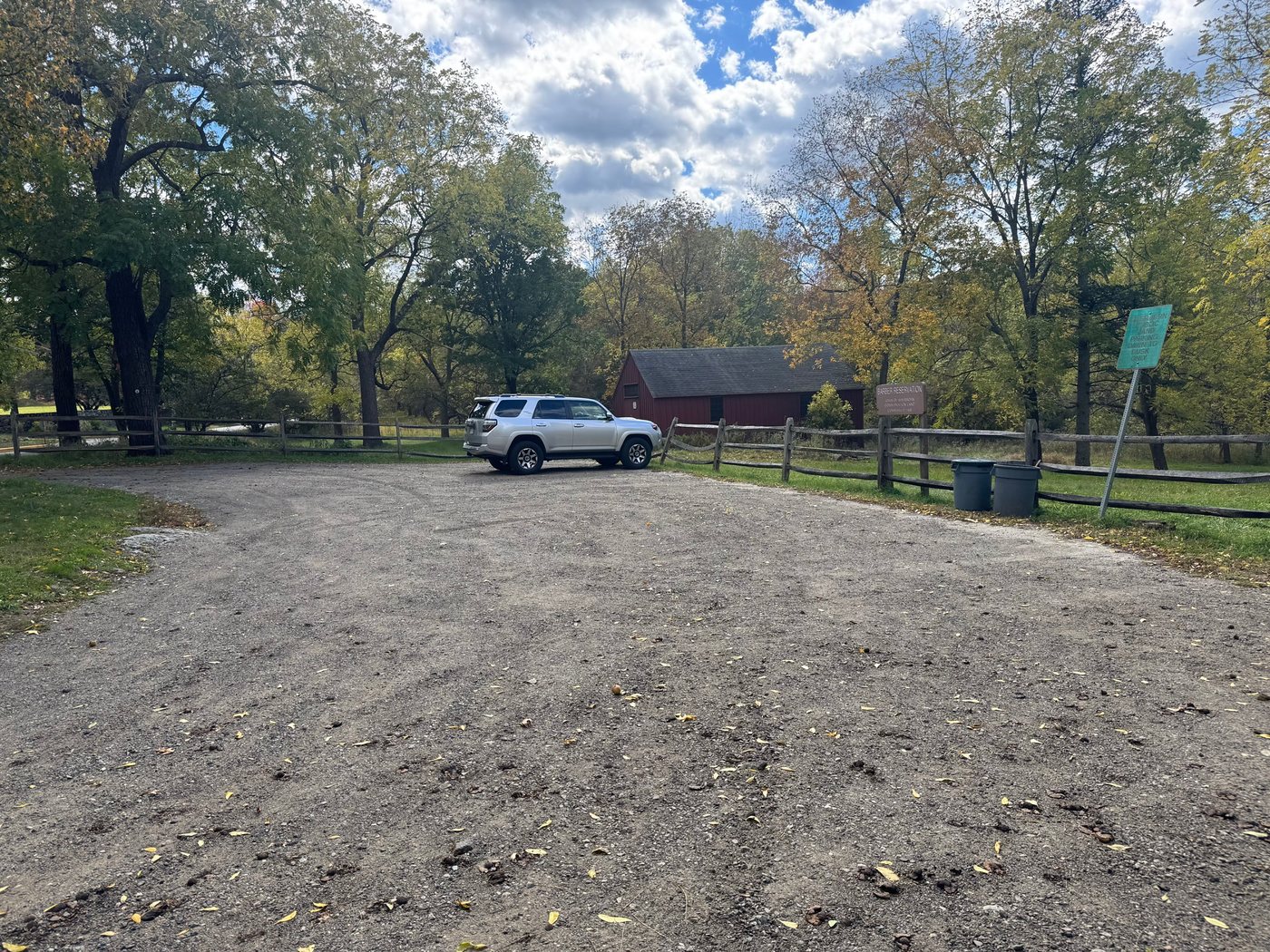 The gravel parking lot at Barber Reservation, with a split-rail fence, the Barber Reservation sign, and a red barn