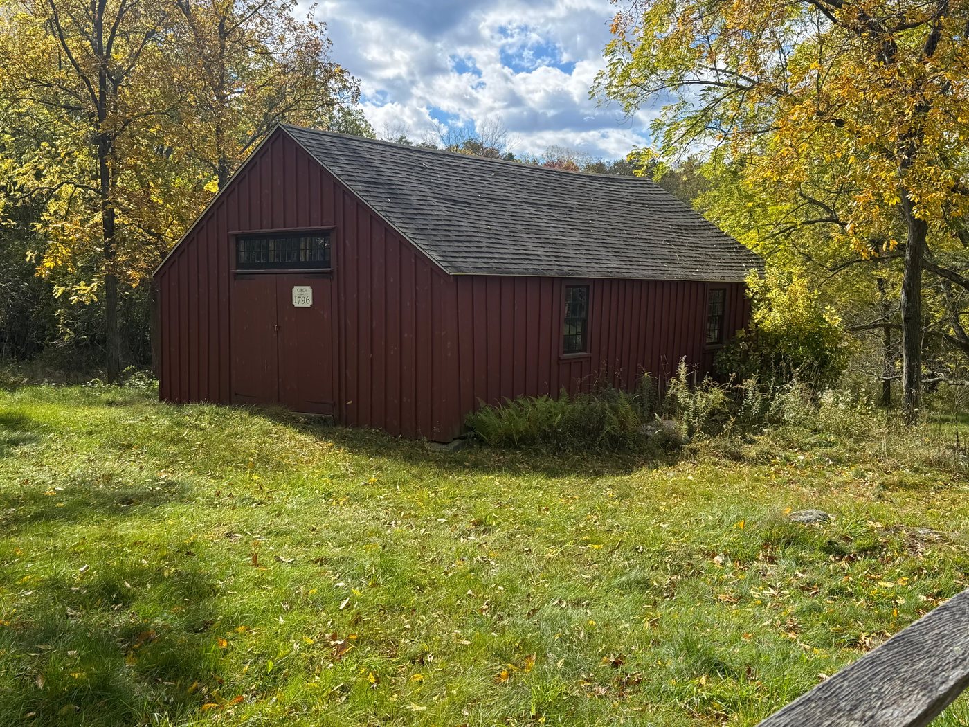 The red board-and-batten barn at Barber Reservation, with a circa 1796 plaque, among yellow fall trees