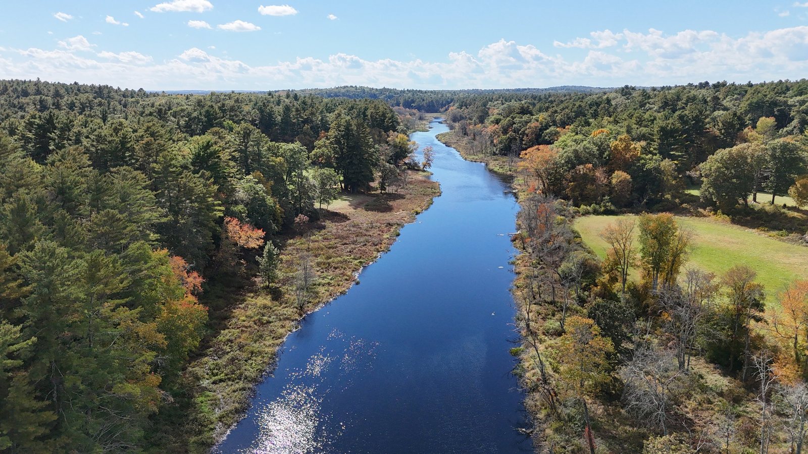 Aerial view of the Charles River winding between wooded banks and an open field in fall