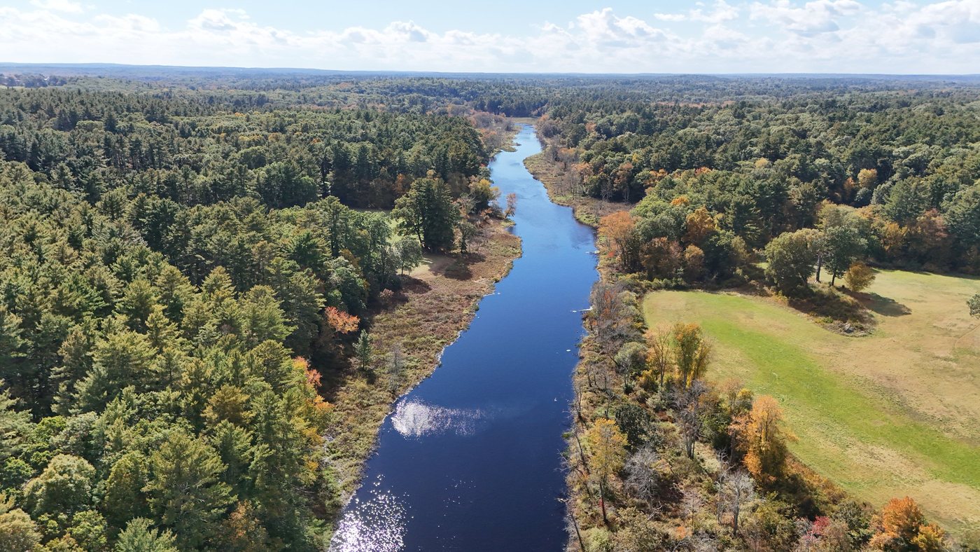 Aerial view of the Charles River winding through woods and past an open field near Sherborn