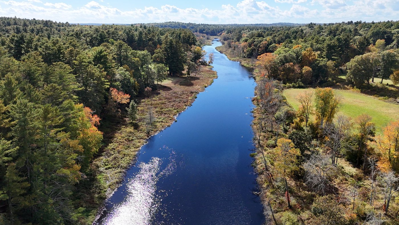 Low aerial view of the Charles River with sun sparkling on the water and fall trees along the banks