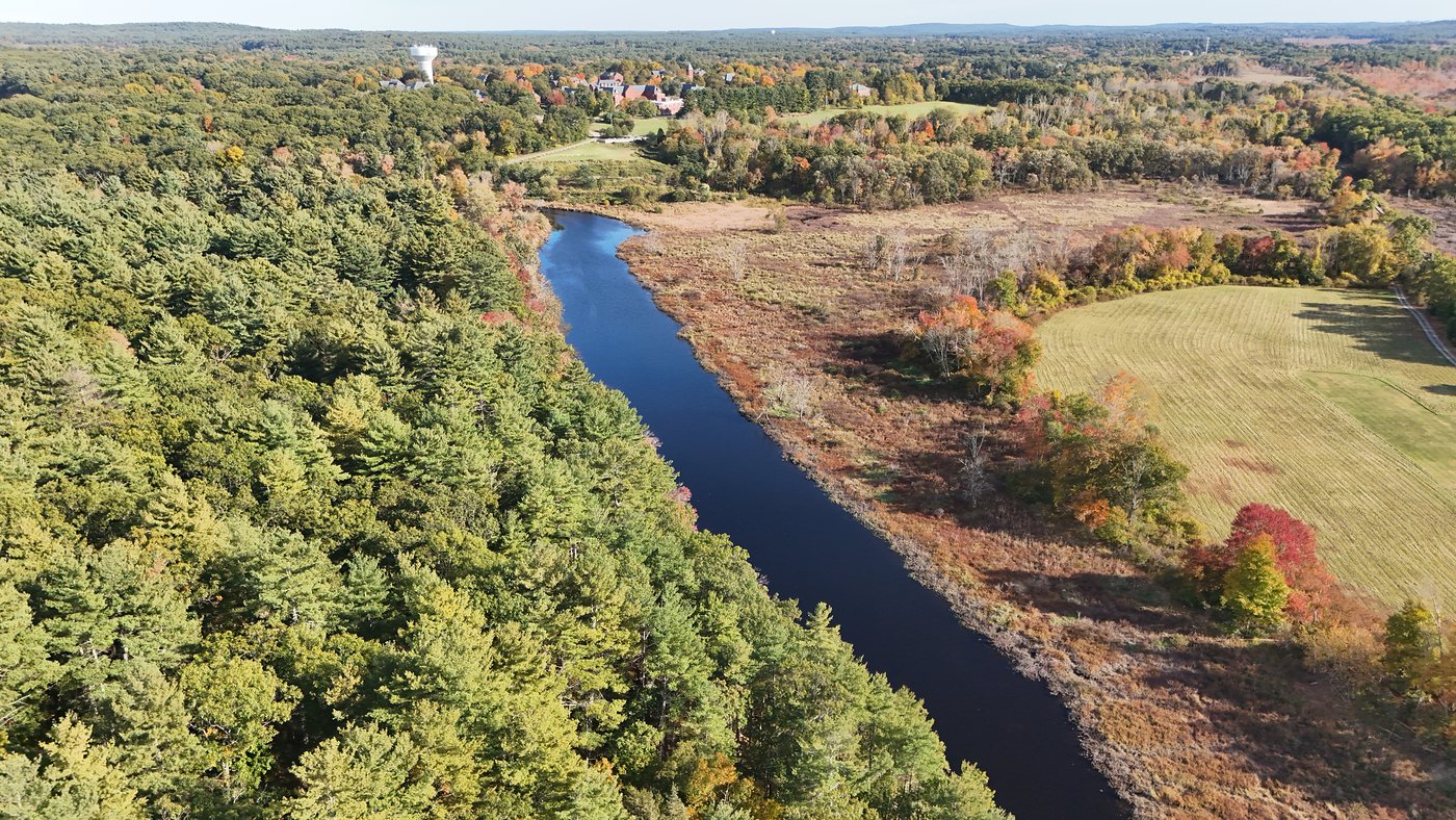 Aerial view of the Charles River in fall below King Philip’s Overlook, with pine woods on one bank and marsh and a mowed field on the other