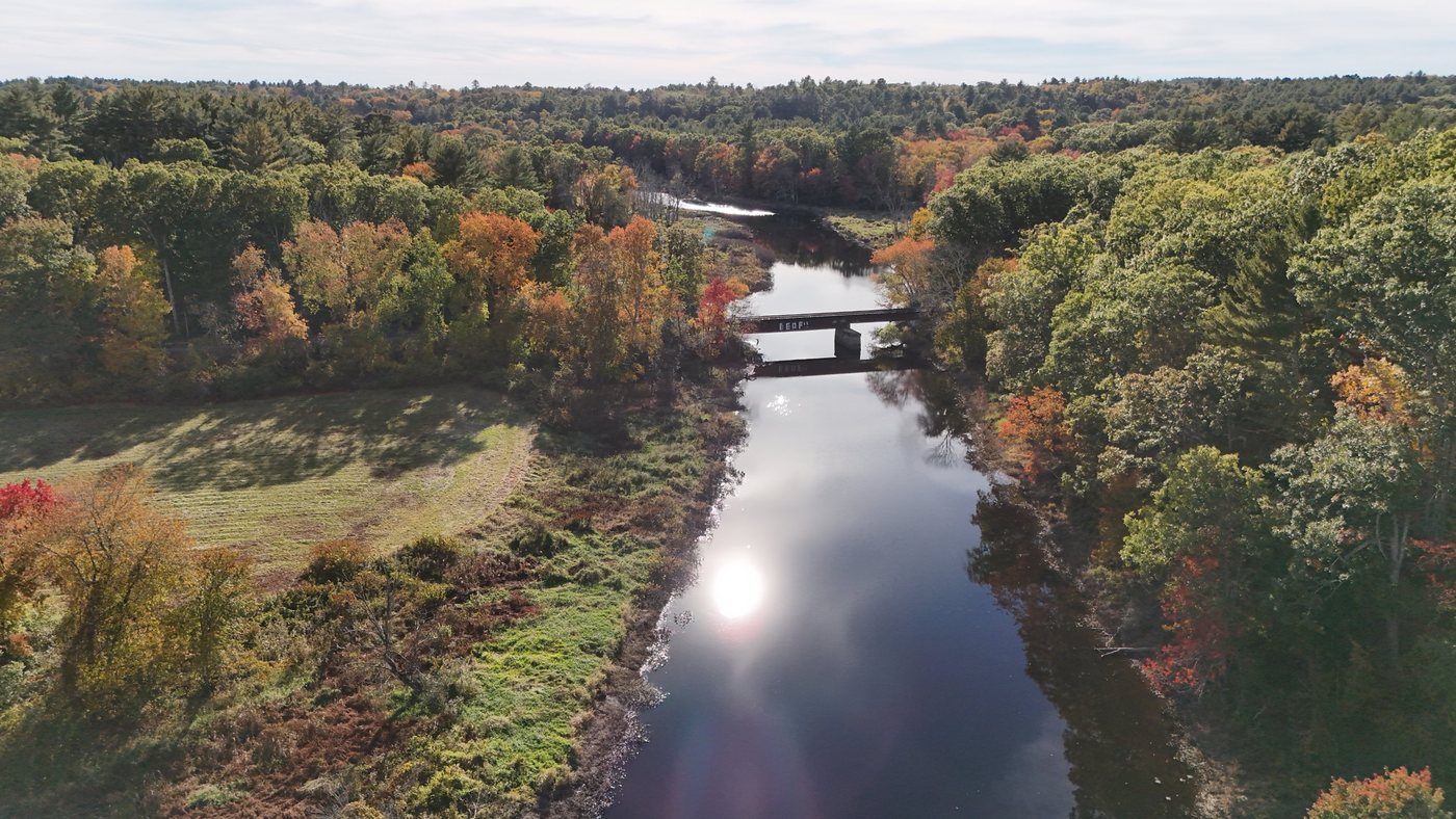 Aerial view of the Charles River in fall, with a railroad bridge crossing it and colorful trees along the banks