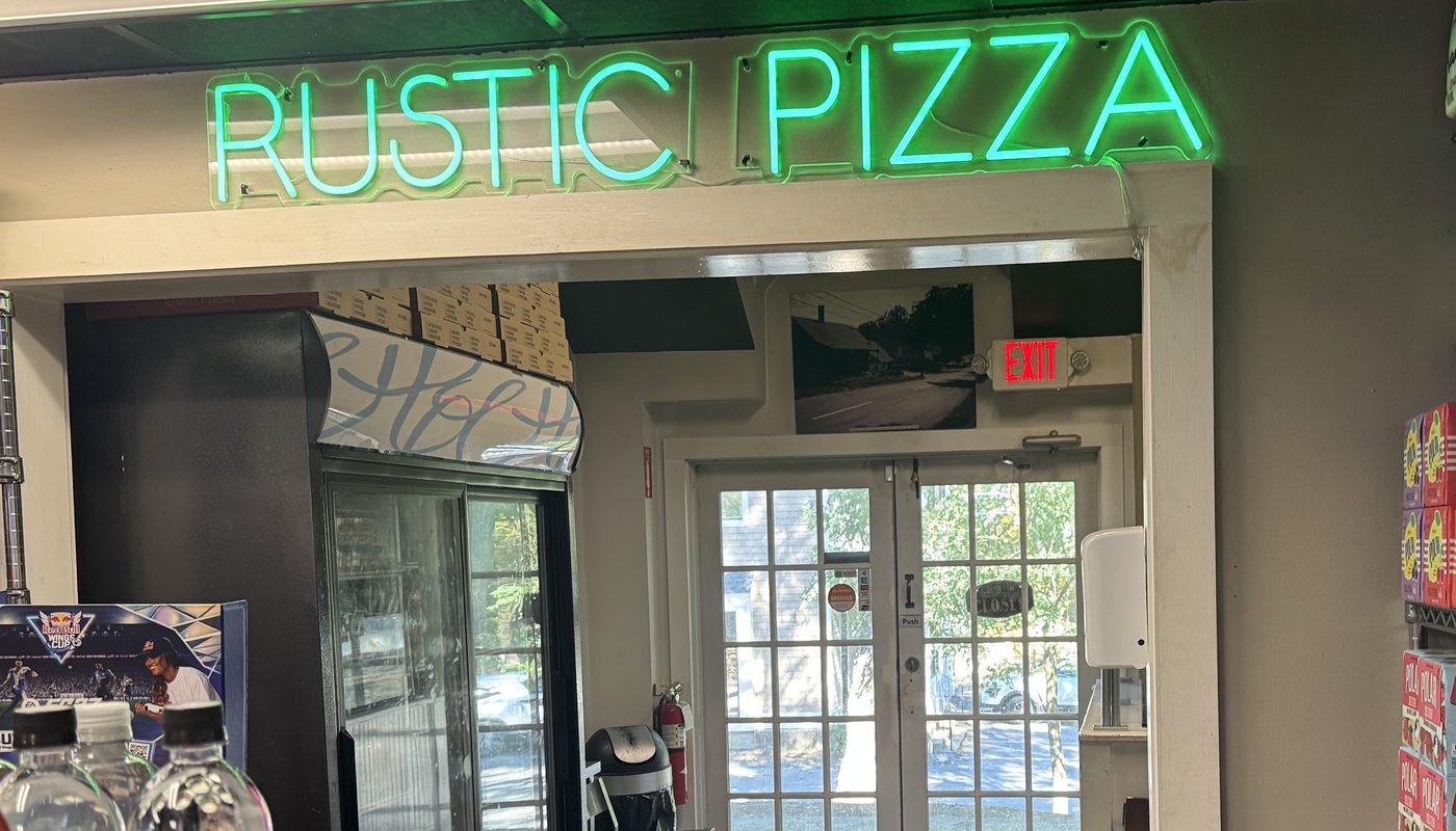 The green neon Rustic Pizza sign over the doorway inside Sherborn Market