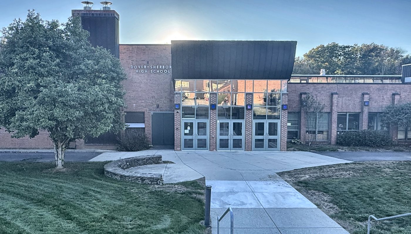 The front entrance of Dover-Sherborn High School, with glass doors under a dark canopy and a walkway across the lawn