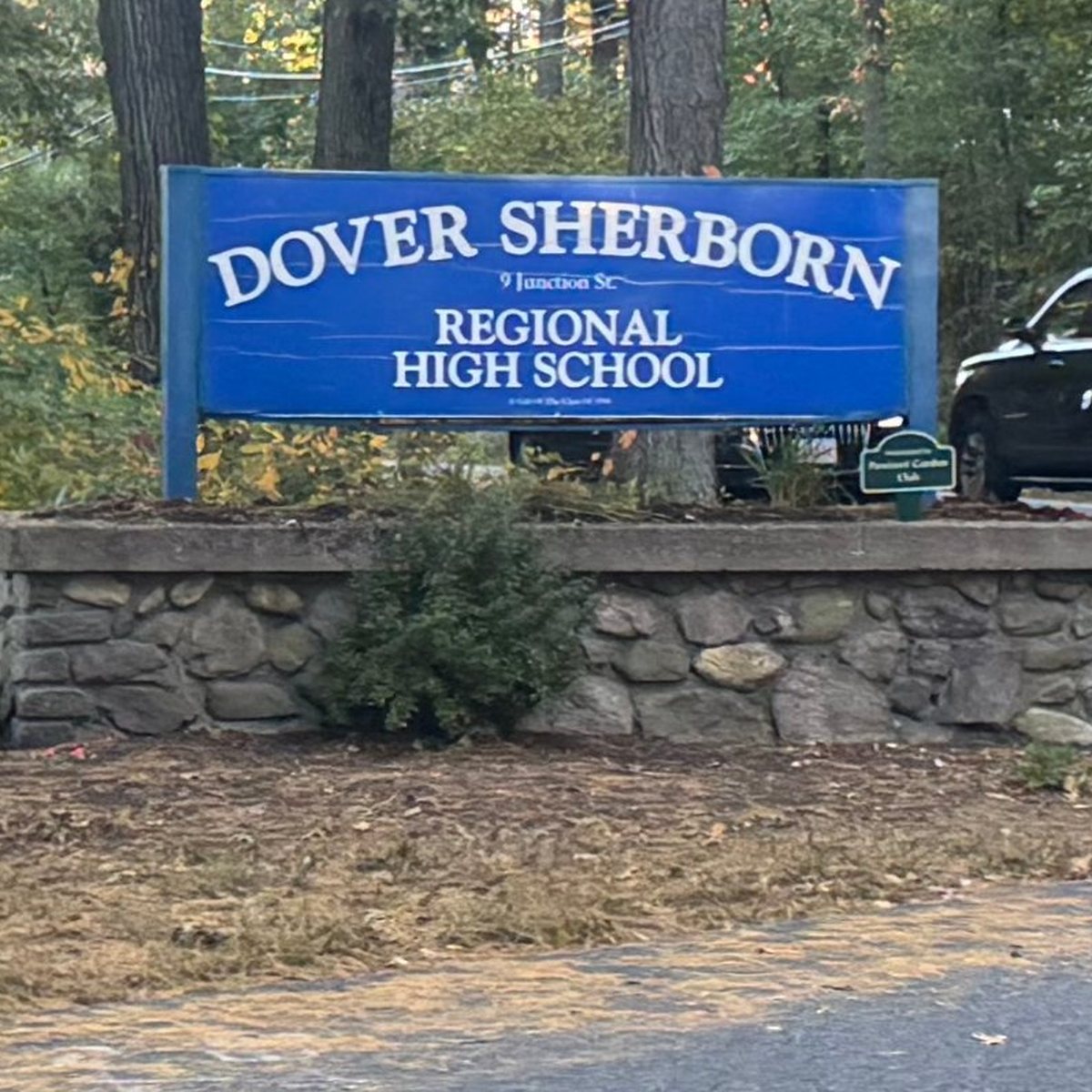 The blue Dover-Sherborn Regional High School sign at 9 Junction Street, on a fieldstone base at the edge of the woods