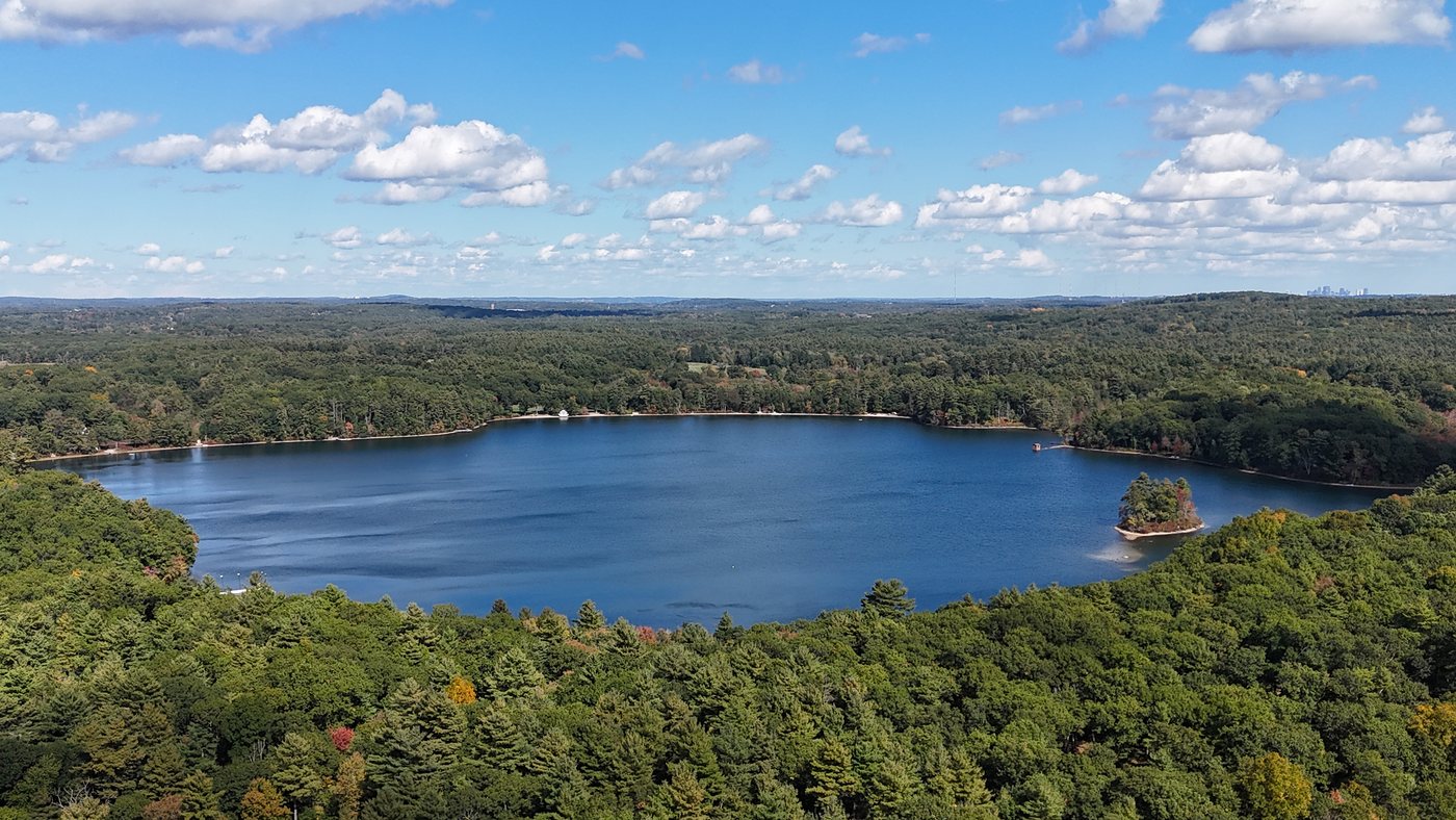 Aerial view of Farm Pond surrounded by woods, with its small island and summer clouds
