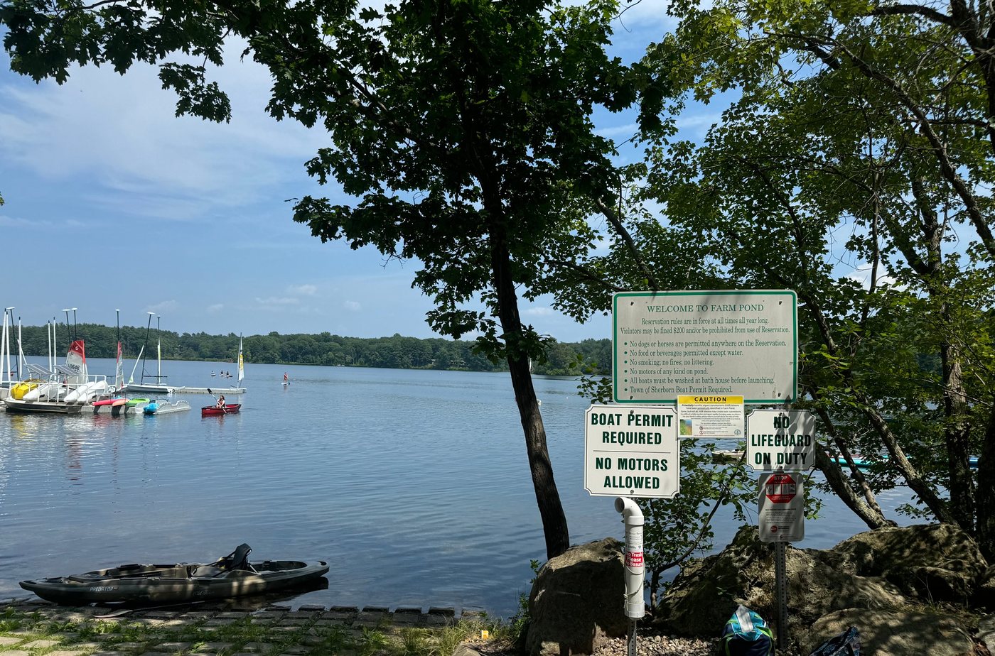 The Farm Pond boat launch with a kayak at the water’s edge, posted pond rules and boat permit signs, and sailboats beyond