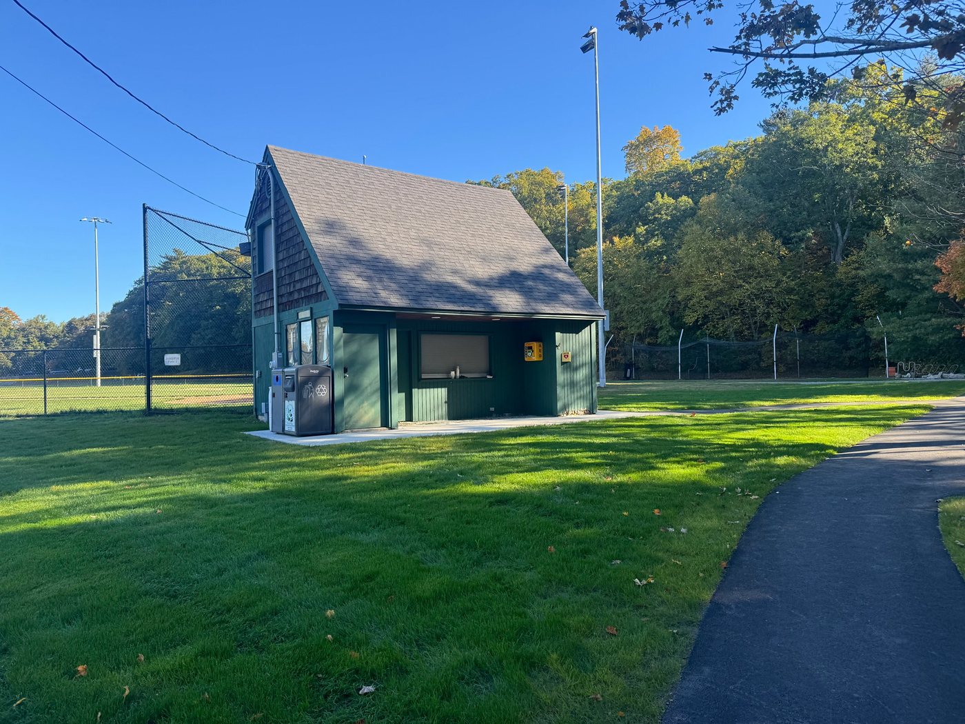 The green concession stand at Jameson Field 1, with an AED mounted on the wall and the backstop and lights beside it
