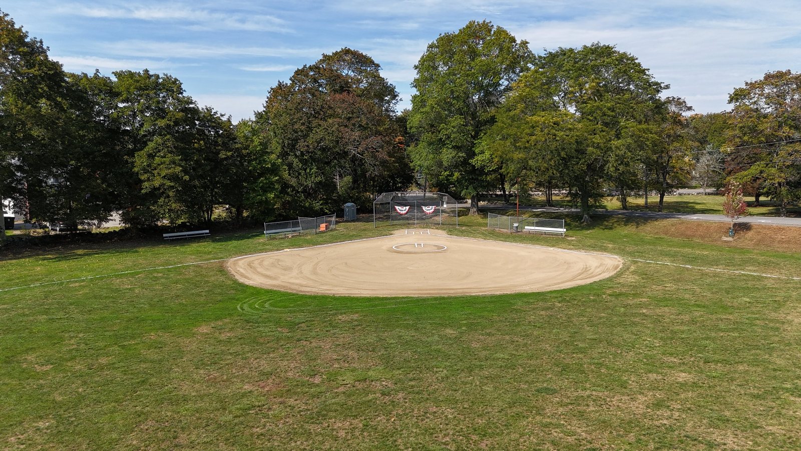 Aerial view of the Jameson softball field, with its all-dirt infield, backstop, and benches, next to Pine Hill Lane
