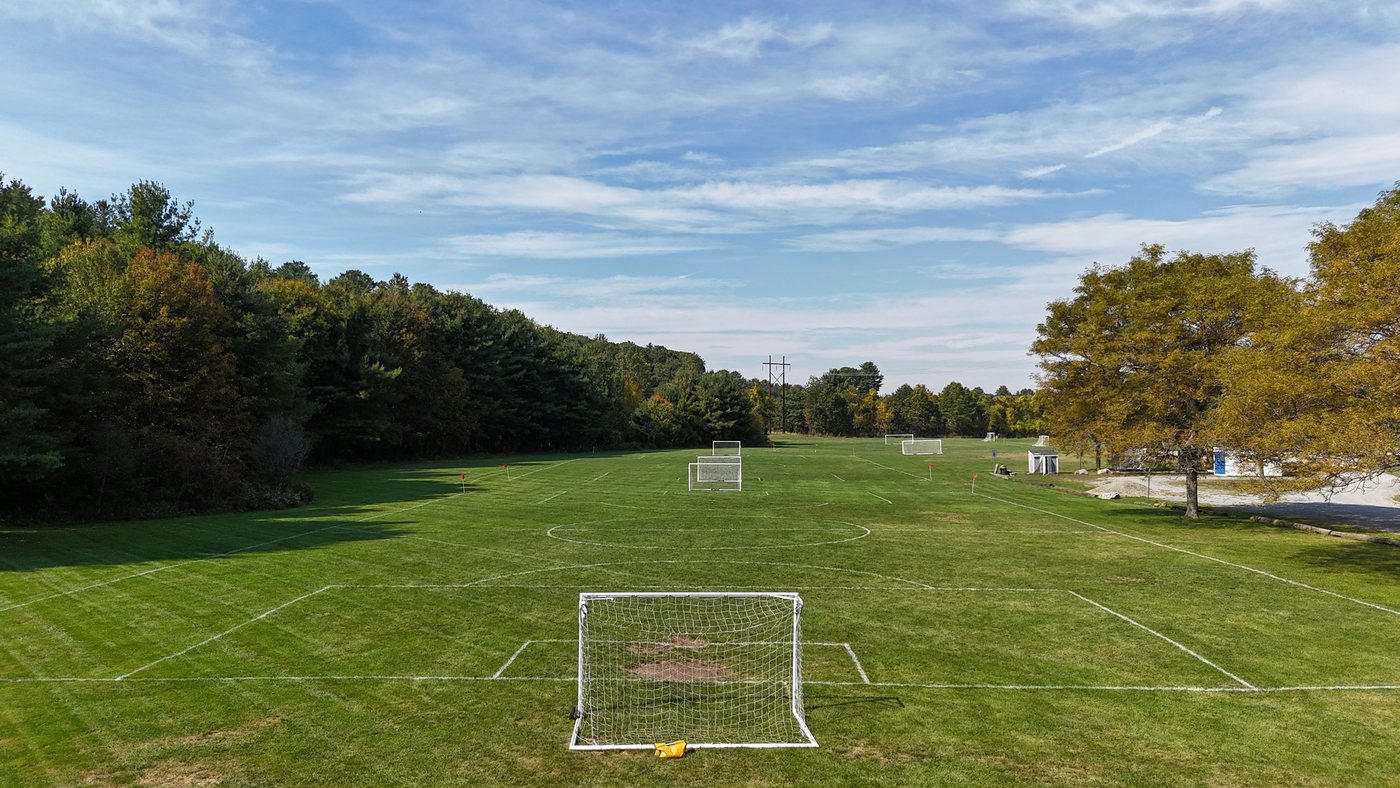 A 7v7 soccer field at Laurel Farm seen from behind the goal, with more fields, goals, and fall trees beyond under a blue sky
