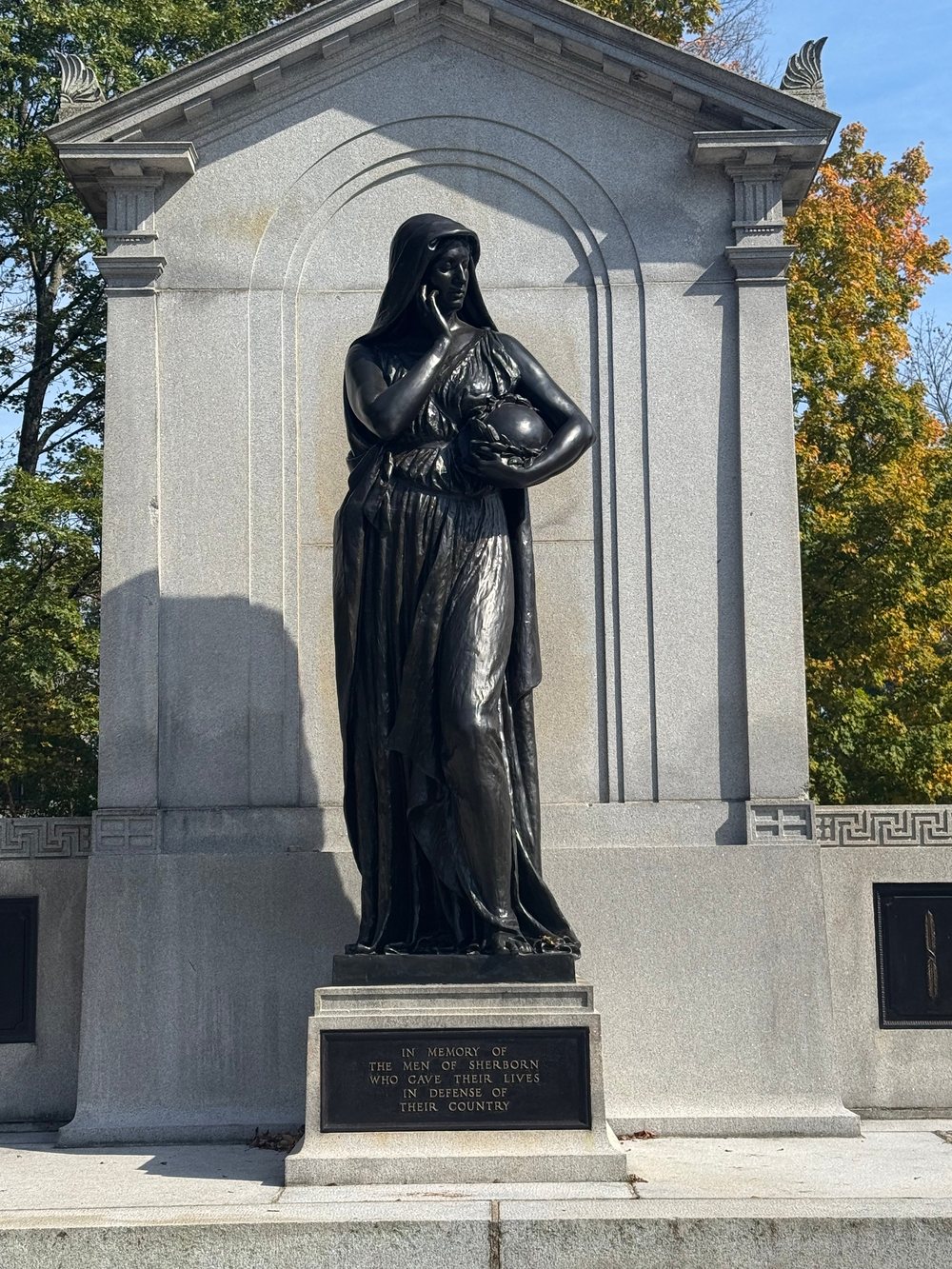 Close-up of the bronze Memory statue, a hooded woman holding a wreathed urn, above a plaque reading “In memory of the men of Sherborn who gave their lives in defense of their country”