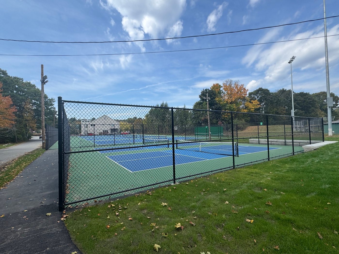 The fenced pickleball and tennis courts seen from the path along Cemetery Lane
