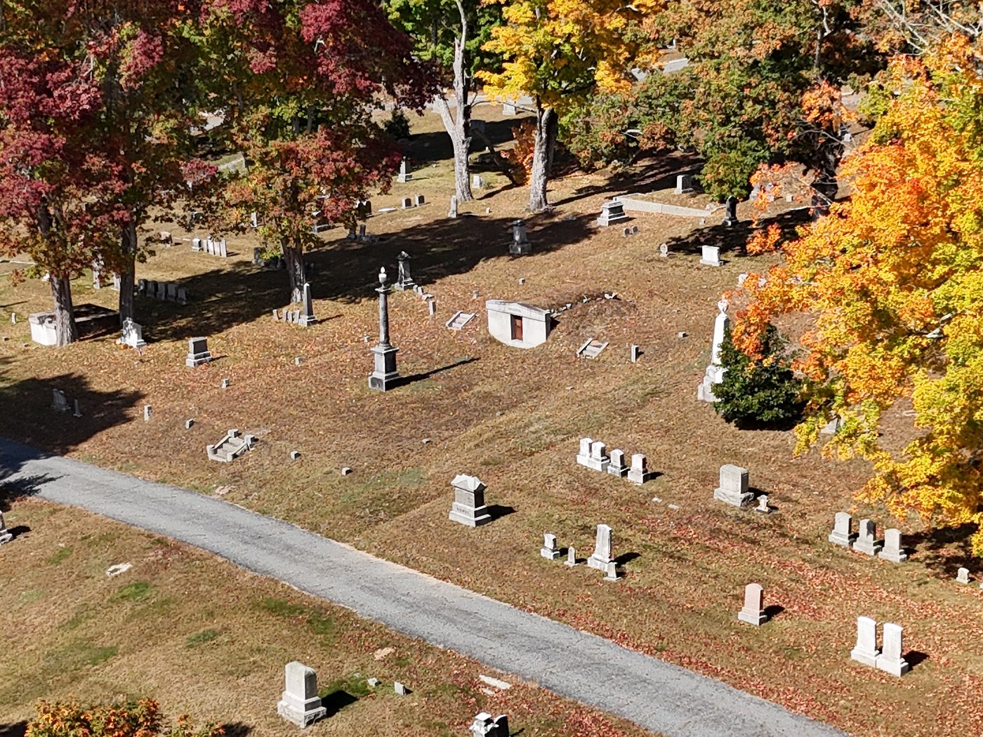 Aerial view of Pine Hill Cemetery in fall, with old monuments, a granite tomb, and red and gold maples along a gravel lane