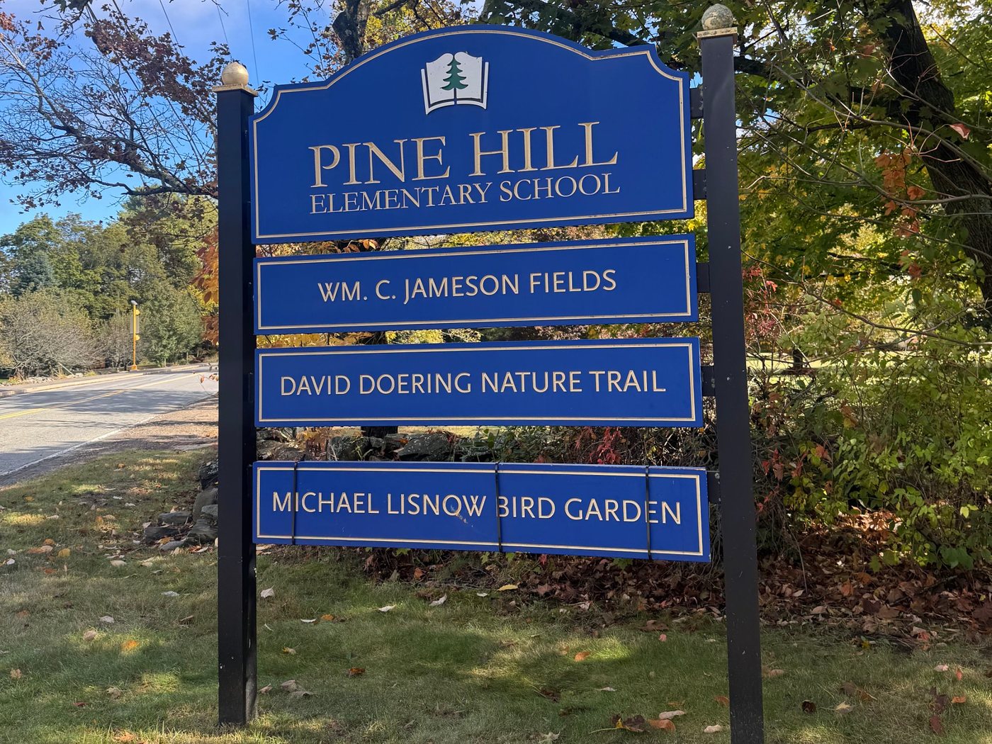 The blue Pine Hill Elementary School sign, with panels for Wm. C. Jameson Fields, the David Doering Nature Trail, and the Michael Lisnow Bird Garden