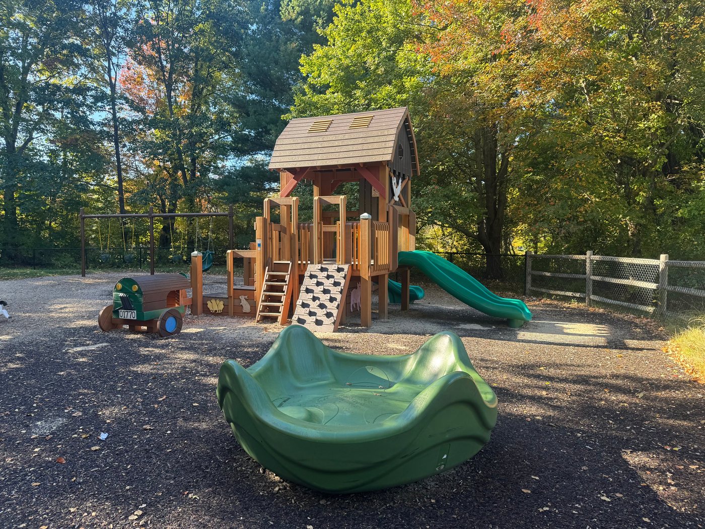 The barn-shaped wooden play structure at Sherborn Playground, with green slides and a climbing wall