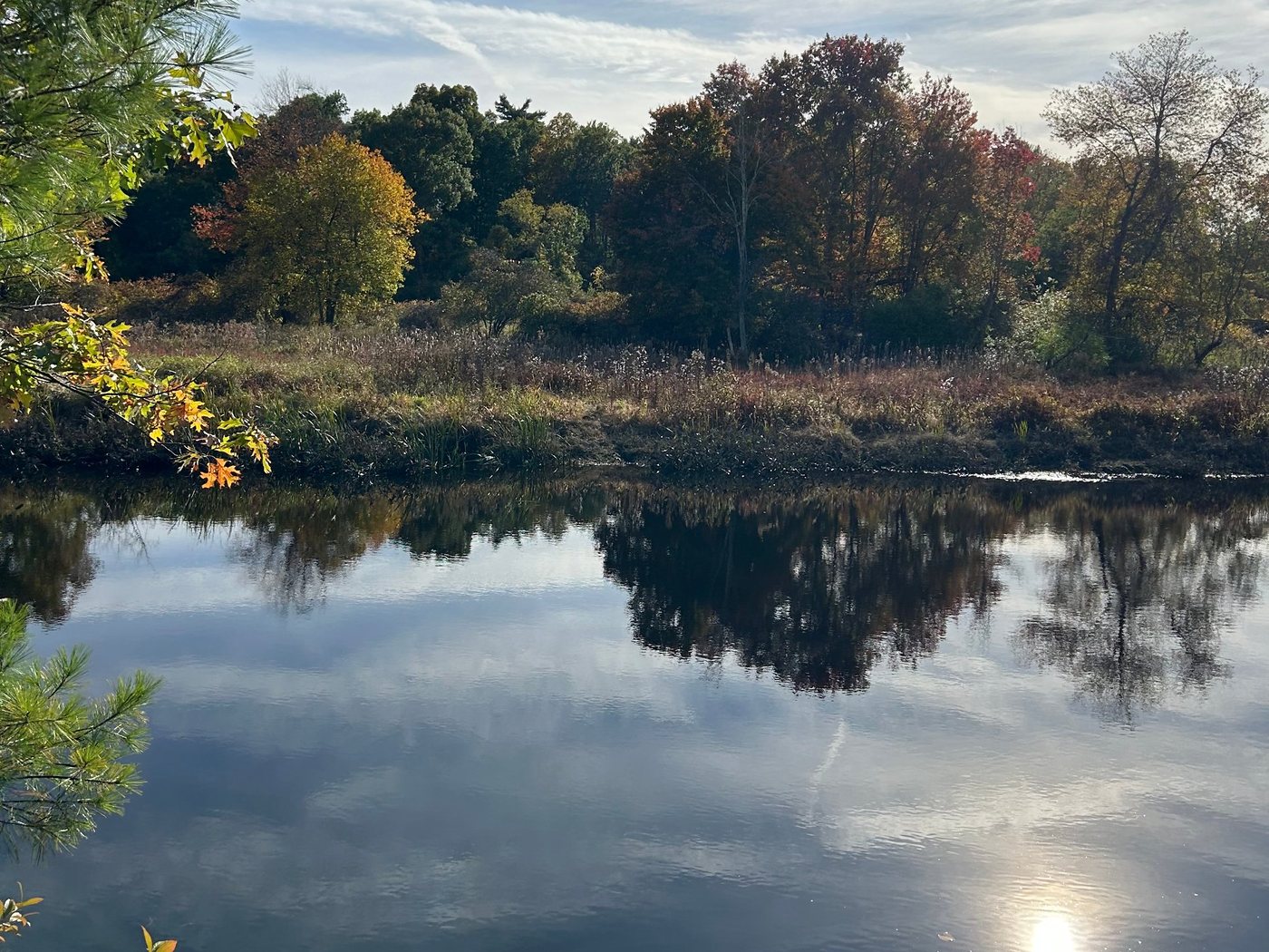 The Charles River at Rocky Narrows in fall, with trees and clouds reflected in still water