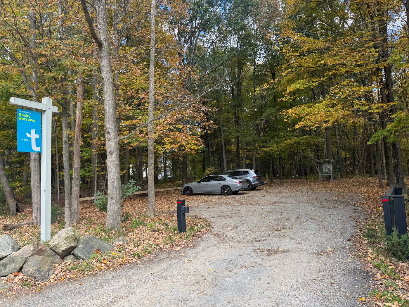 The small gravel parking lot off Route 27 under fall trees, with the trailhead kiosk at the back