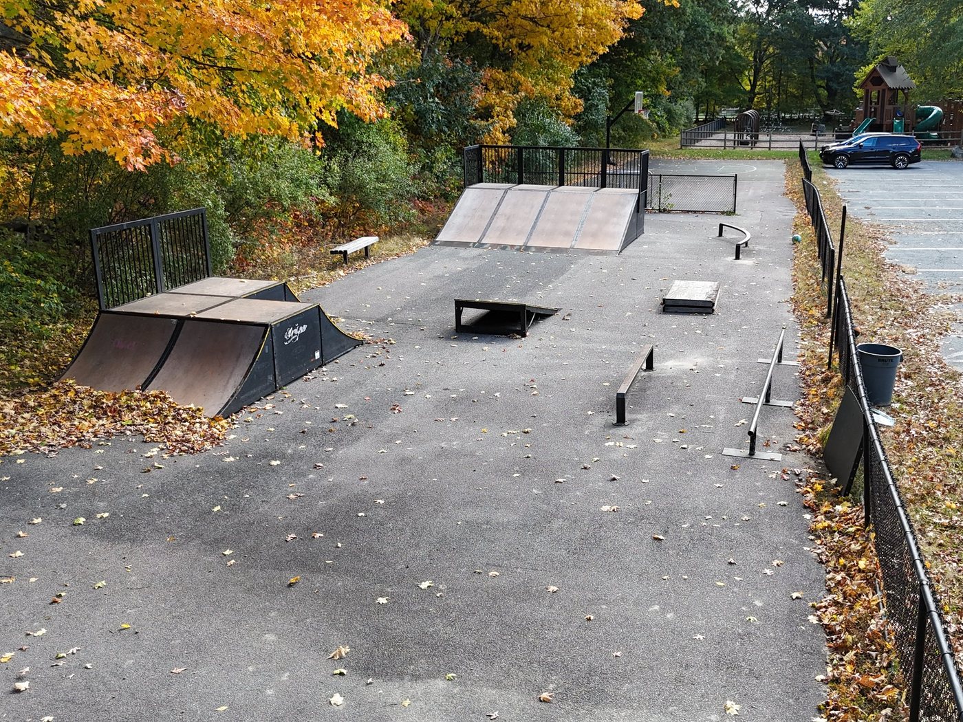 The outdoor skate park in the Ward J. Parks Recreation Area, with quarter pipes, ramps, rails, and a box under fall maples, and Sherborn Playground beyond