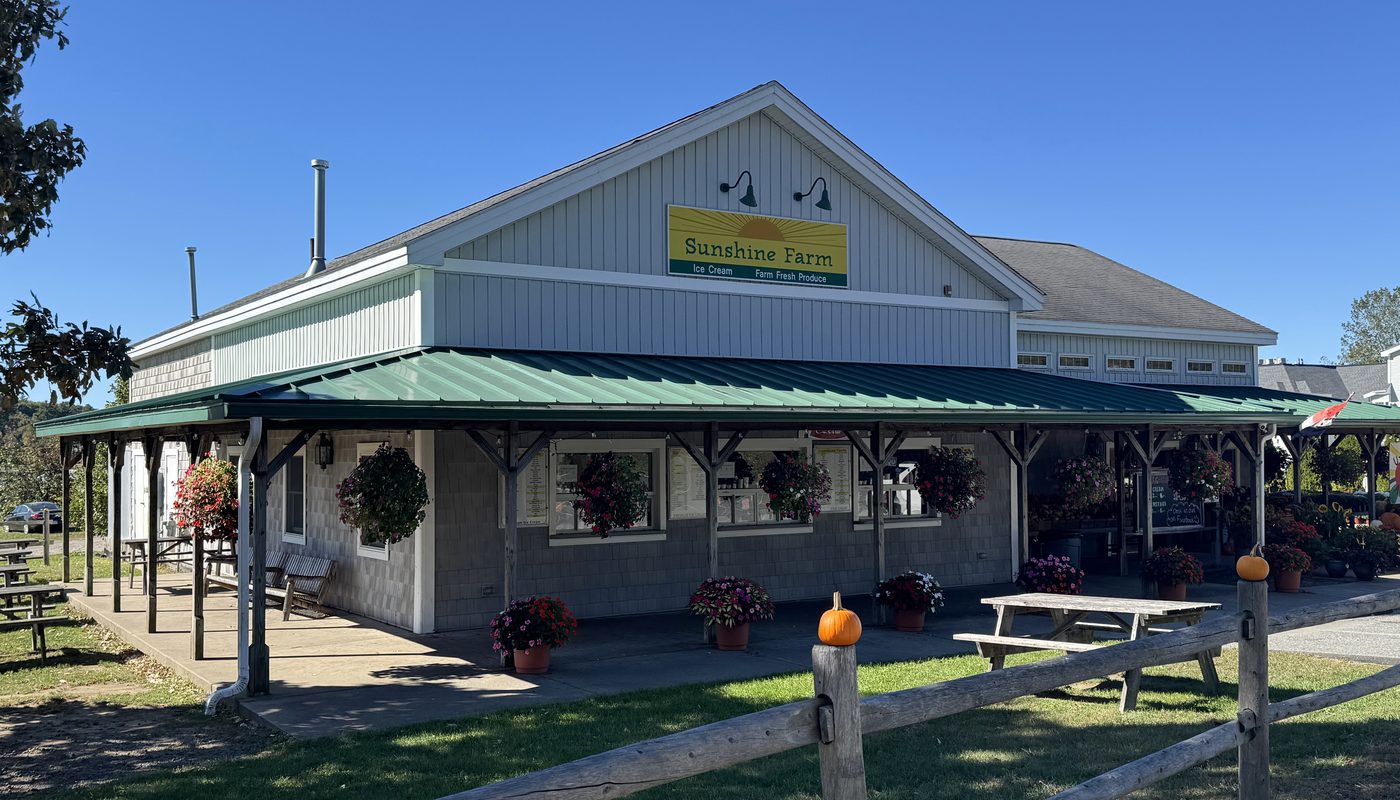 The Sunshine Farm stand, with its yellow sign, green porch roof, hanging flower baskets, and picnic tables