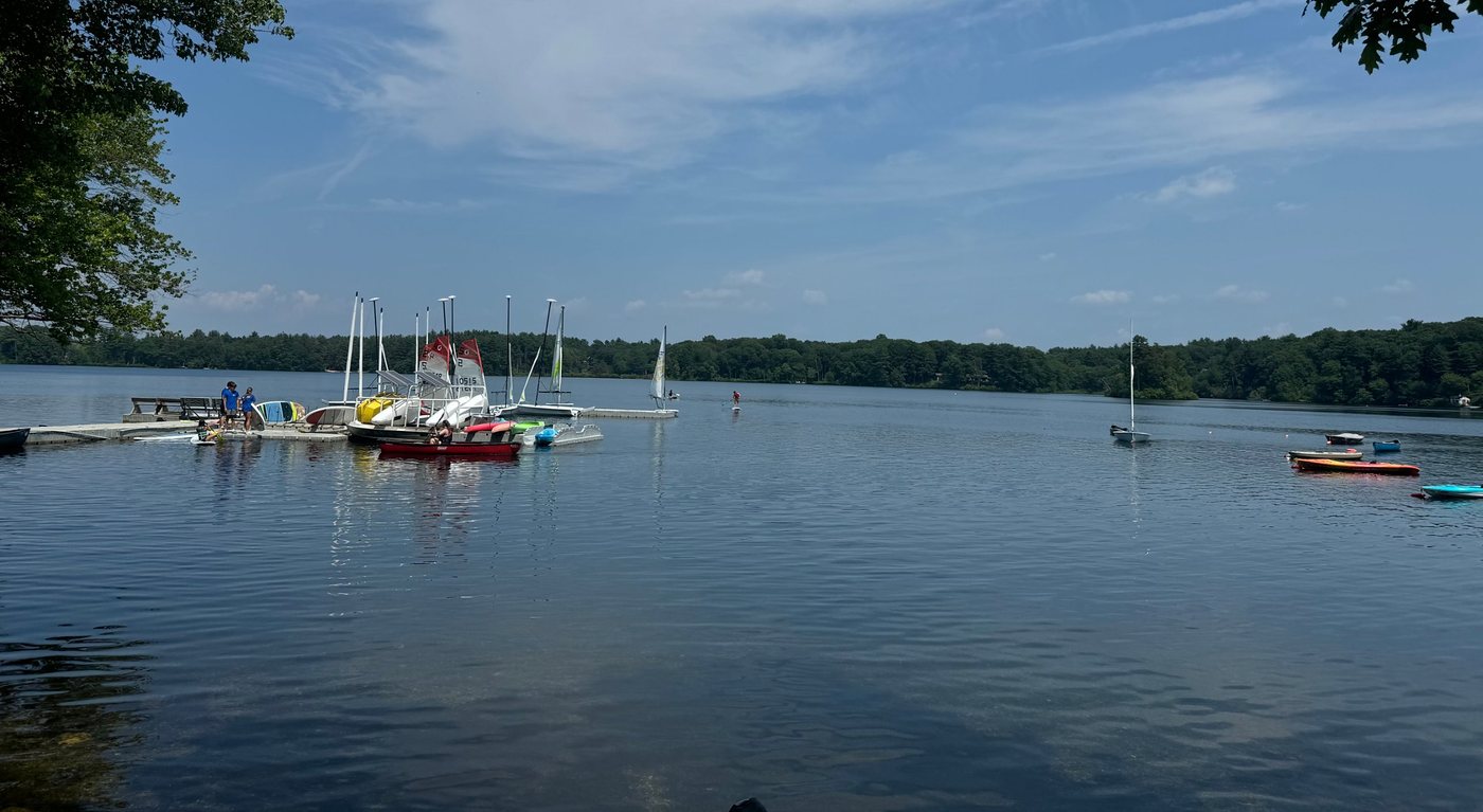 Sherborn Yacht Club sailboats, kayaks, and paddleboards at the club docks on Farm Pond on a summer day, with sailors out on the water