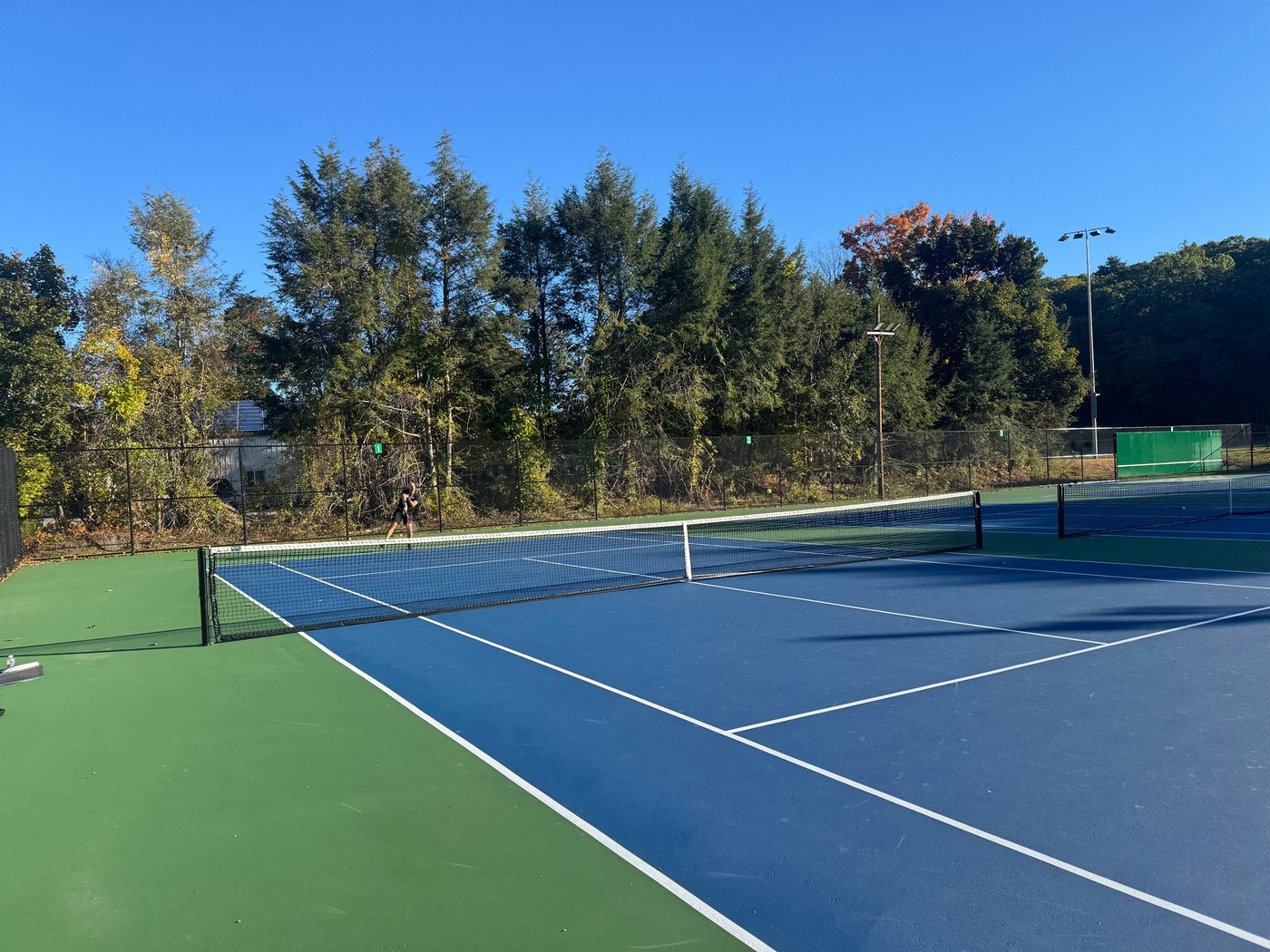A local resident playing tennis on one of the blue and green courts on a sunny fall day