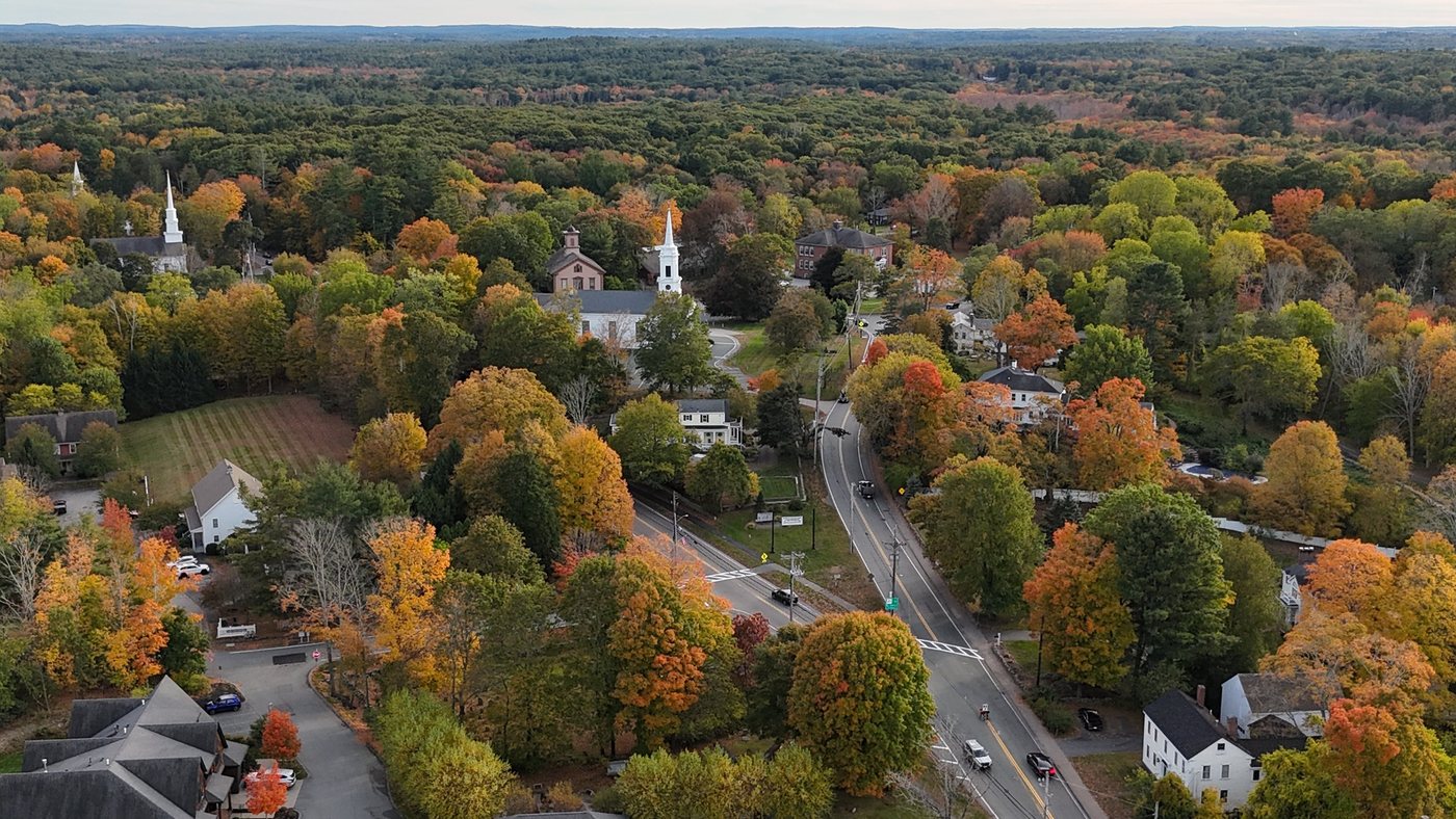 Aerial view of Sherborn’s town center in fall, where Routes 16 and 27 split, with Town Hall, the 1858 Town House, white steeples, and colorful trees